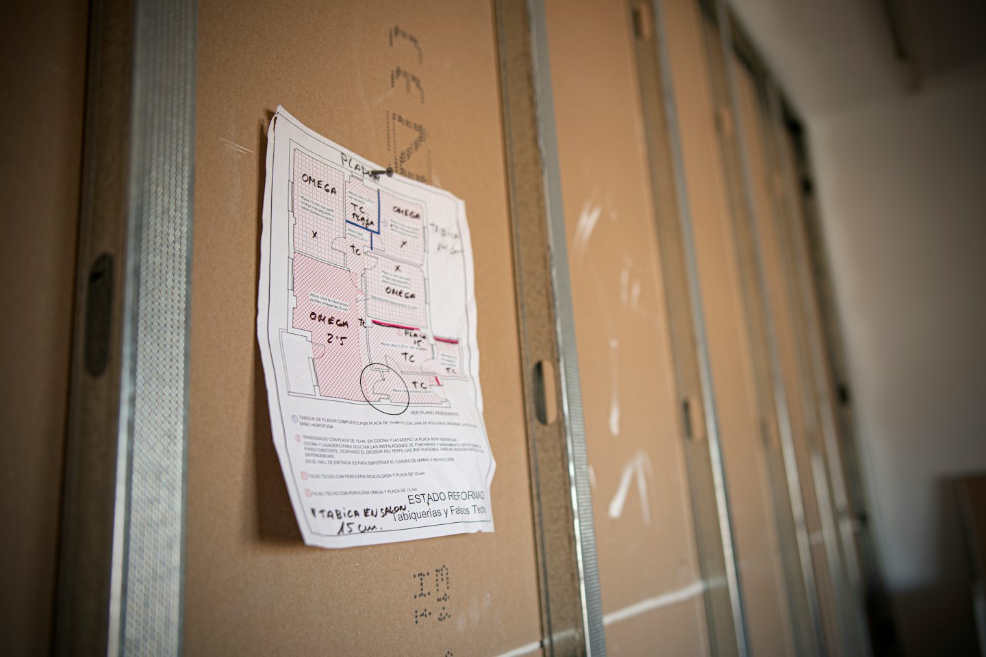 Construction blueprint with red markings pinned to a wood panel.